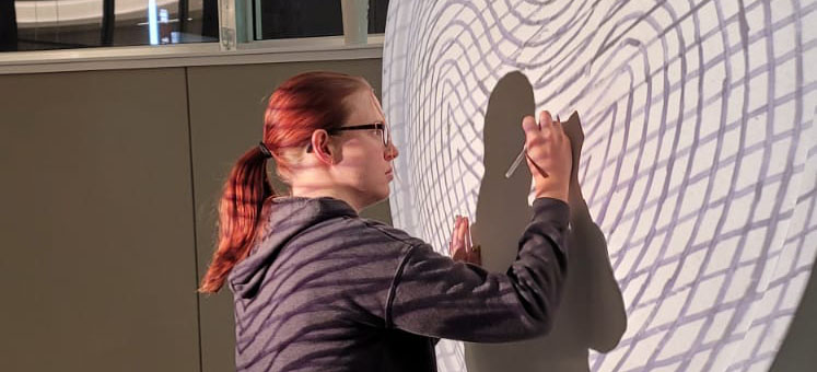 Woman with a paintbrush on a large sculpture with projected lines